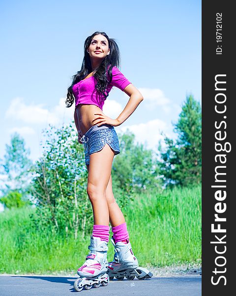 Happy young brunette woman on roller skates in the park