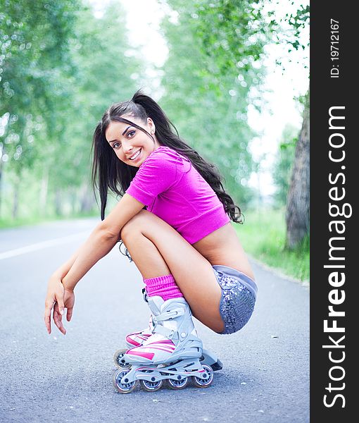 Happy young brunette woman on roller skates in the park