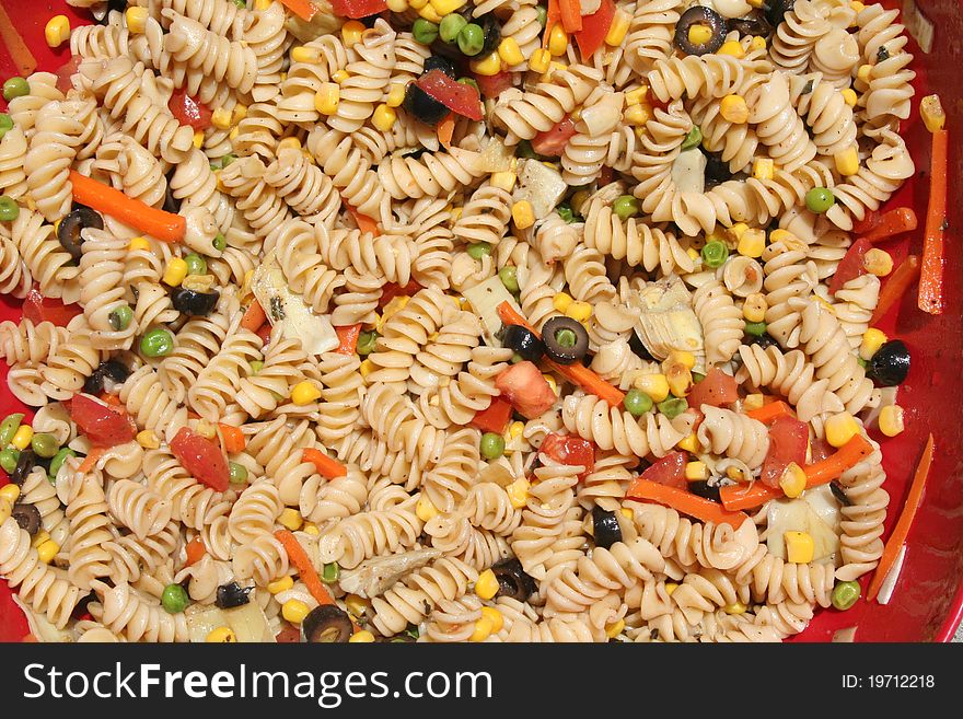 Red bowl filled with colorful pasta salad.
