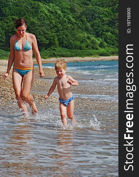Happy family of mother with kid running on the sea beach