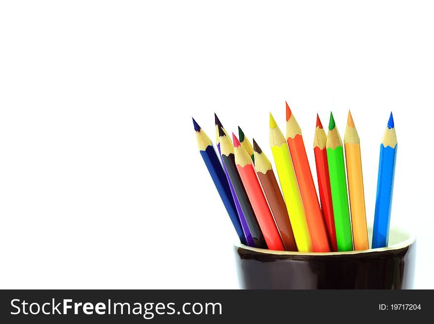 Various color pencils in black cup on white background.