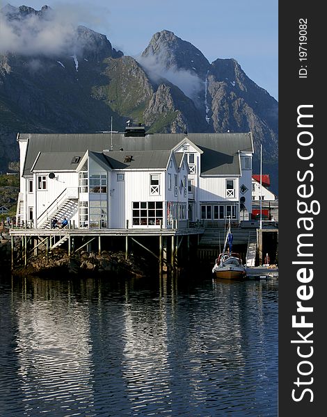 Wooden hotel standing on pillars over the sea with high mountains in the background in Lofoten. Wooden hotel standing on pillars over the sea with high mountains in the background in Lofoten