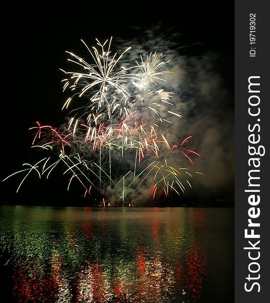 Colorful fireworks on the black sky background and water reflections