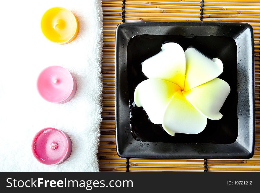 Three candles on white towel with plumeria in the plate on bamboo mat