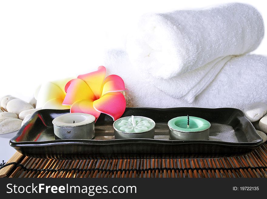 Three candles in ceramic bowl and white towel on bamboo mat.