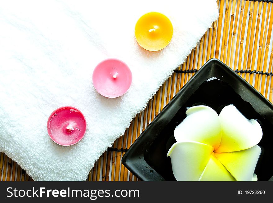 A plumeria in the plate and three candles with white towel on bamboo mat.