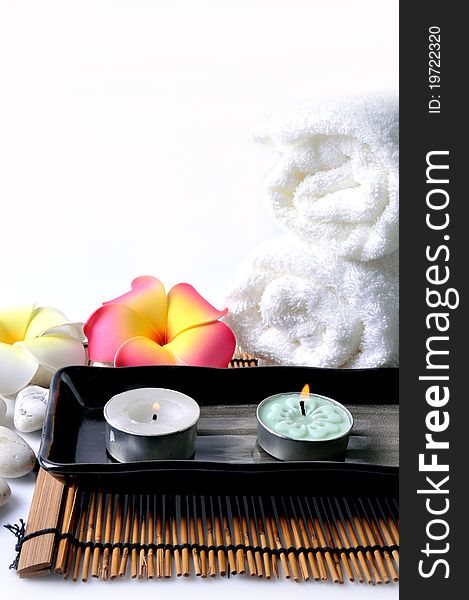 Two candles in ceramic bowl and white towel on bamboo mat.