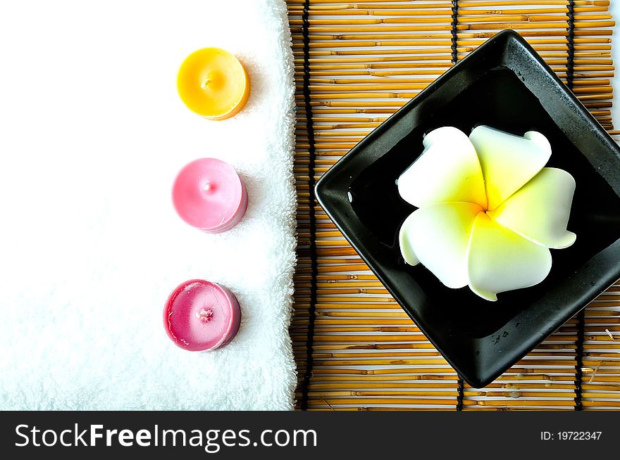 A plumeria in the plate and three candles with white towel on bamboo mat.