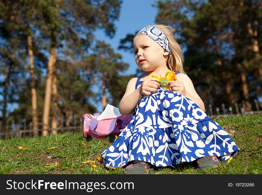 Little girl is sitting on grass and keep flower