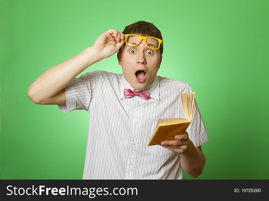 Young attractive man in a shirt and yellow glasses, bow tie on a green background reads the yellow book. Bookworm. Young attractive man in a shirt and yellow glasses, bow tie on a green background reads the yellow book. Bookworm