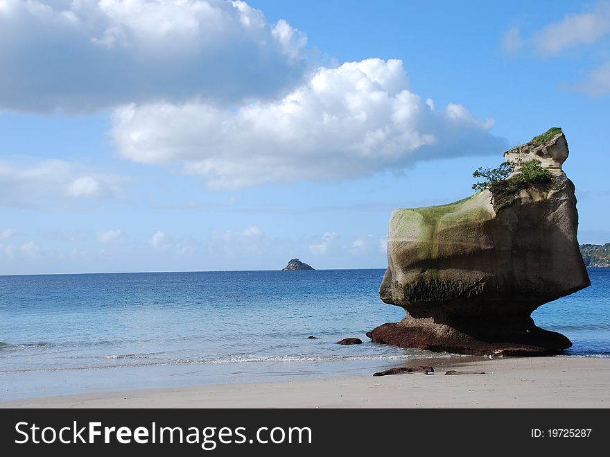 Pristine white-sand beach with moss-covered rock formation against a blue sky with fluffy white clouds. Pristine white-sand beach with moss-covered rock formation against a blue sky with fluffy white clouds.