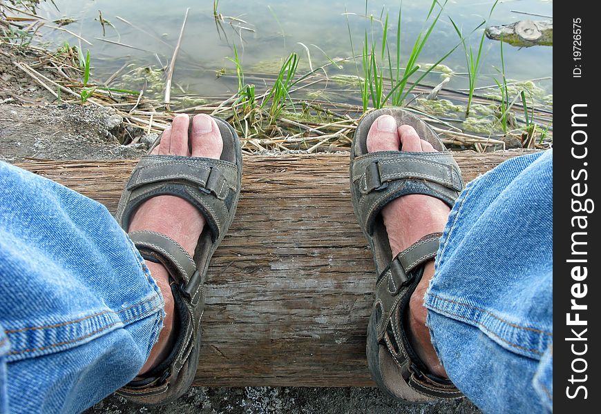 A mans levis covered legs and sun burnt feet in sandals. A mans levis covered legs and sun burnt feet in sandals