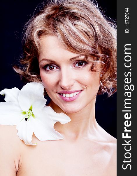 Beautiful young blond woman  with a lily in her hair, against black background