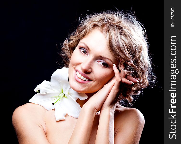 Beautiful young blond woman  with a lily in her hair, against black background