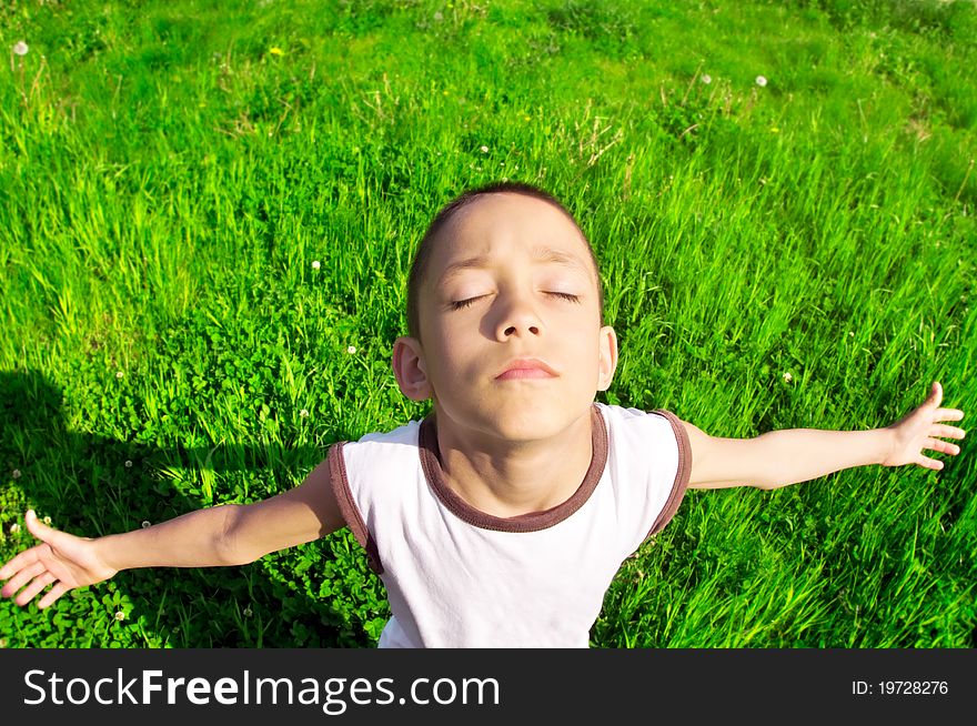 Boy with outstretched hands relaxing in the field under the sunlight. Boy with outstretched hands relaxing in the field under the sunlight