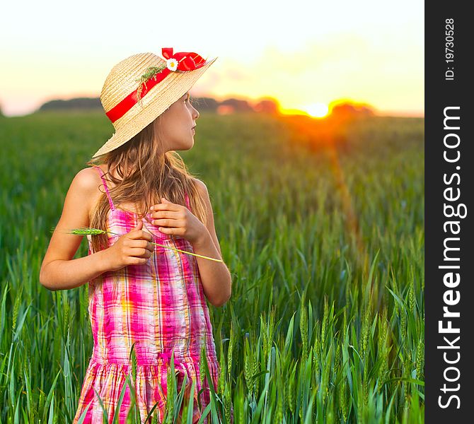 Cute girl in the straw hat with red ribbon on green wheat. Cute girl in the straw hat with red ribbon on green wheat.