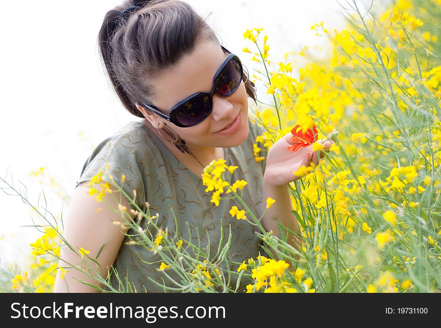 Brunette girl with a corn poppy in her hand, on a blooming rapeseed, canola field