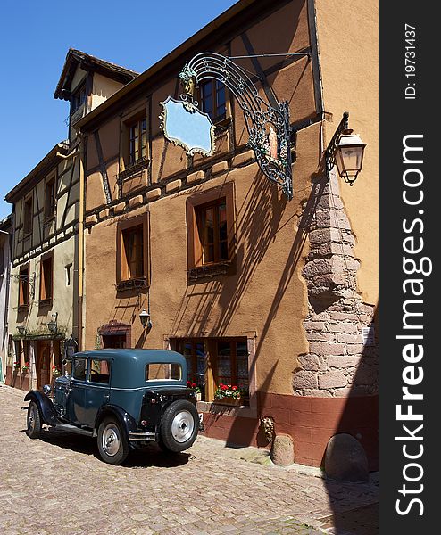 French traditional house with half-timbered wall. La route du vin â€“ route of vines â€“ village in Alsace - France. An old car in front of a restaurant. French traditional house with half-timbered wall. La route du vin â€“ route of vines â€“ village in Alsace - France. An old car in front of a restaurant.