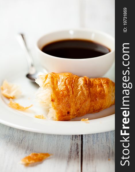 Croissantand a cup of black coffee on a white plate. Croissantand a cup of black coffee on a white plate