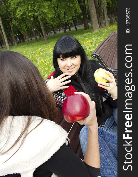 Mother and daughter in a park sitting on a wooden bench eating apples