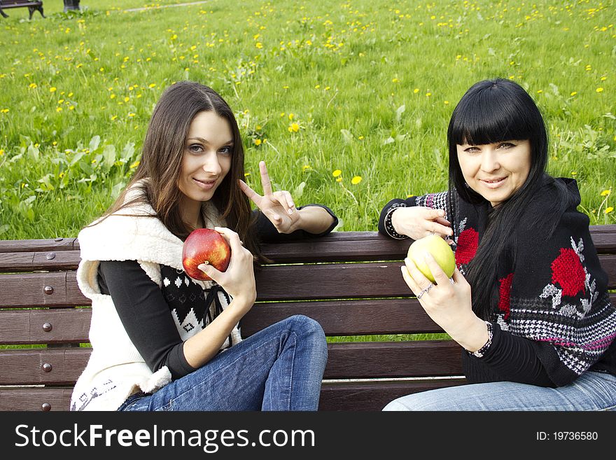 Mother and daughter in a park sitting on a wooden bench eating apples