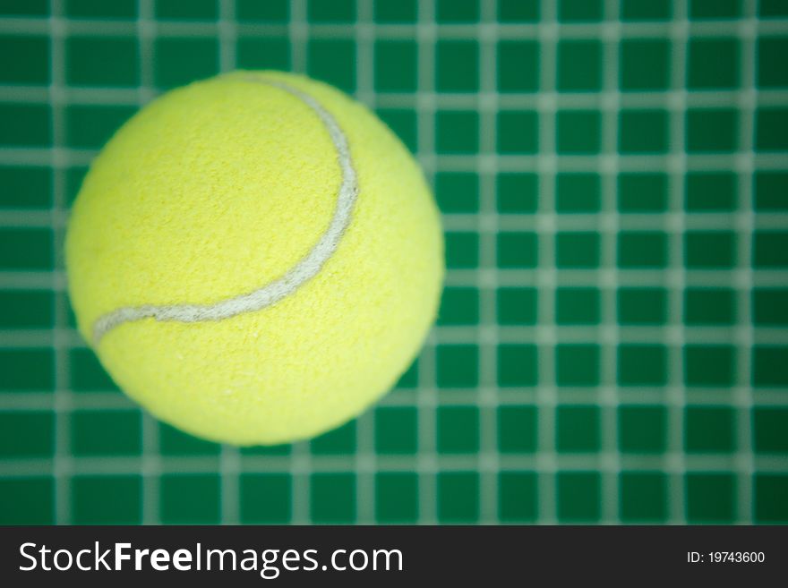The tennis ball of green color lies on a grid from a tennis racket. The tennis ball of green color lies on a grid from a tennis racket
