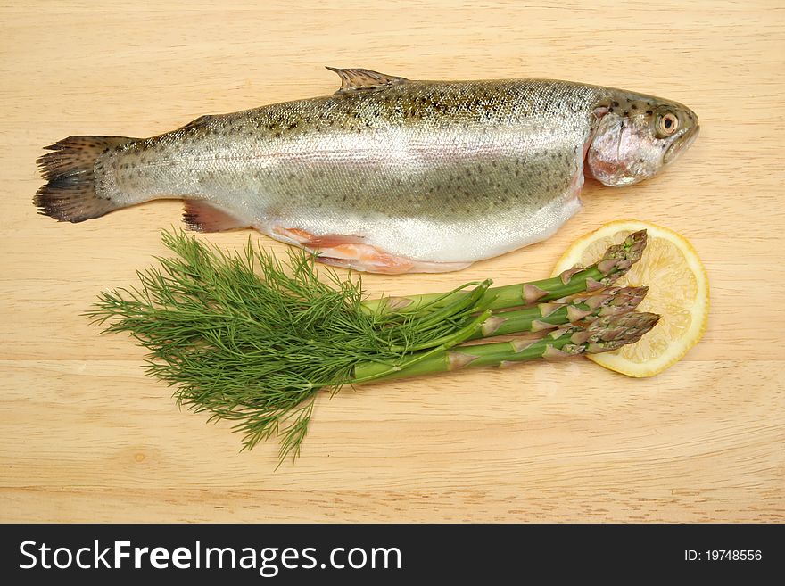 Fresh rainbow trout with dill herbs, asparagus and lemon on a wooden food preparation board. Fresh rainbow trout with dill herbs, asparagus and lemon on a wooden food preparation board