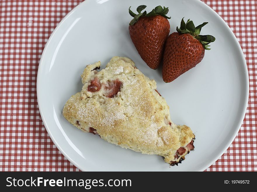 A sugar-topped strawberry scone sits on a light blue plate next to two fresh strawberries. A sugar-topped strawberry scone sits on a light blue plate next to two fresh strawberries.