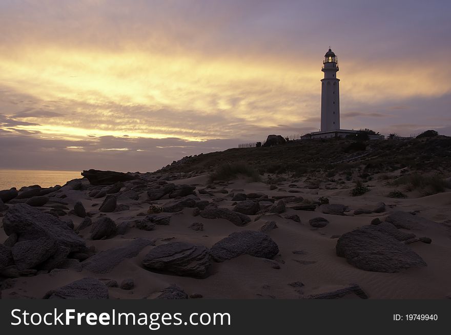 A photo of a lighthouse taken whilst the sun was setting from the beach making everything look like a silhouette. A photo of a lighthouse taken whilst the sun was setting from the beach making everything look like a silhouette