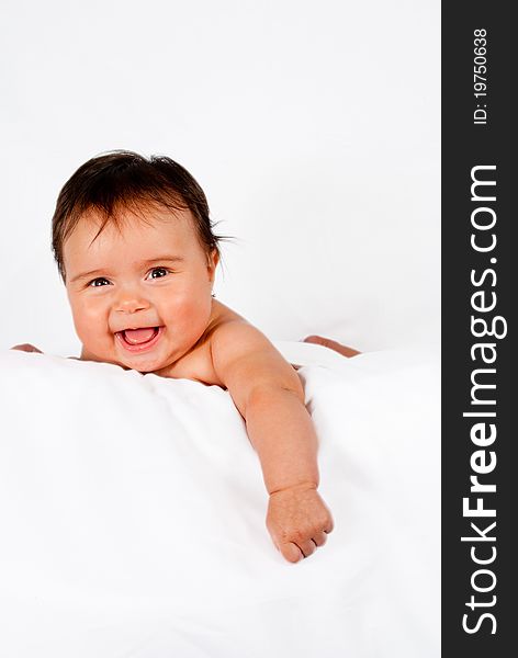 A mixed ethnicity baby smiles while laying on a white pillow and background.