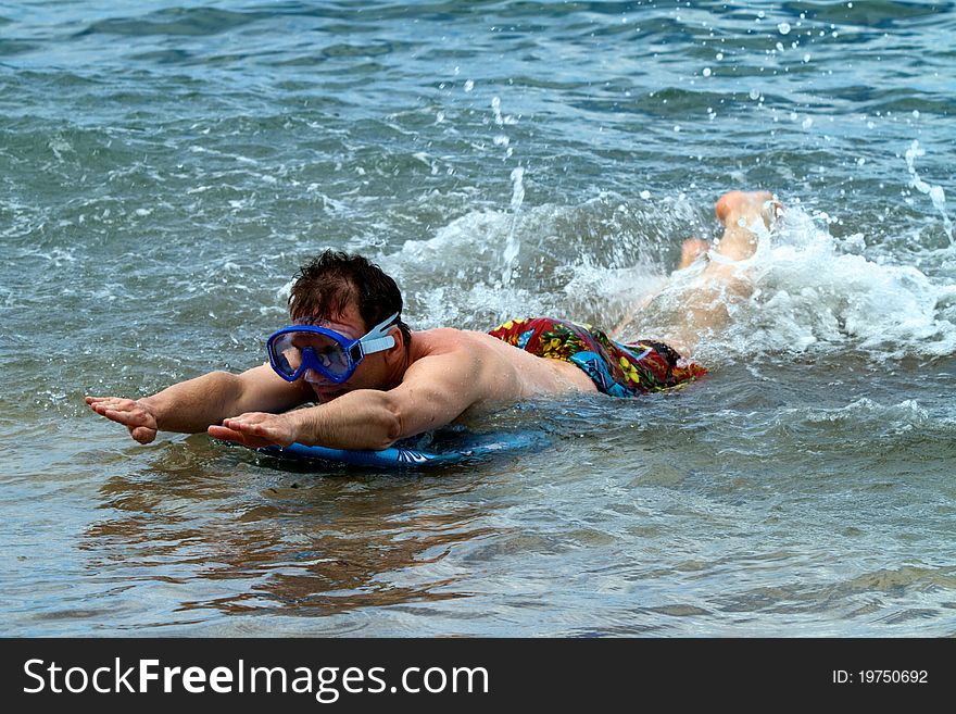A man wears a diving mask while body boarding at the beach.