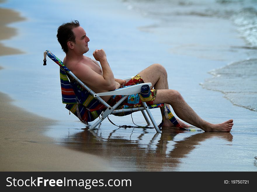 A man is deep in thought while sitting in a lawn chair at the edge of the shore at a Maul beach.