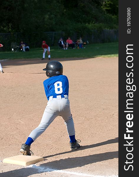A Little League player wearing a blue and gray uniform with a black helmet stretches off the base getting ready to run in a game in Salem, Oregon in 2010. A Little League player wearing a blue and gray uniform with a black helmet stretches off the base getting ready to run in a game in Salem, Oregon in 2010