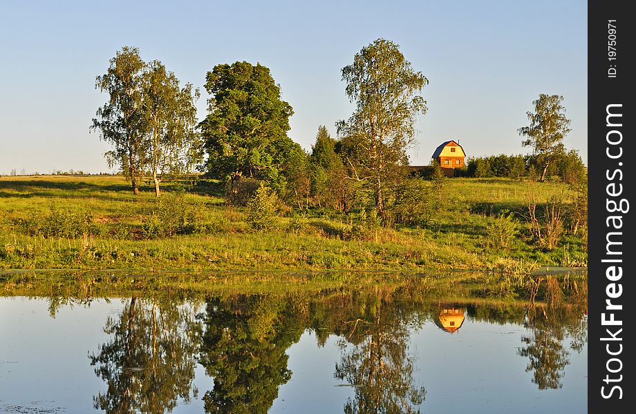 Country summer landscape with small house on lake bank and trees reflections, evening. Country summer landscape with small house on lake bank and trees reflections, evening