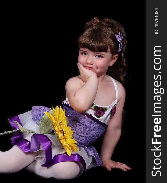 Smiling sweet little girl in purple and white ballet outfit sitting with sunflower. isolated on black. Smiling sweet little girl in purple and white ballet outfit sitting with sunflower. isolated on black