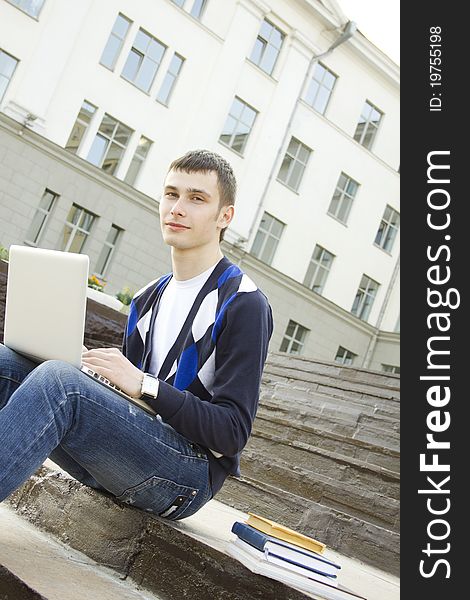 Close-up young attractive student studies on a with books and laptop in a college campus. Sitting on the stairs of the building. Close-up young attractive student studies on a with books and laptop in a college campus. Sitting on the stairs of the building