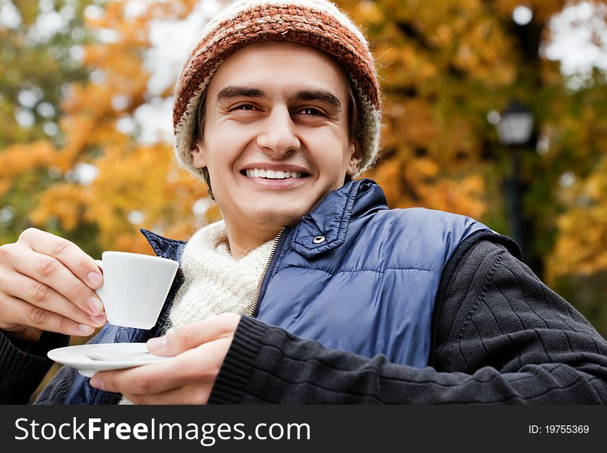 Close-up of smiling young man holding a cup of coffee in autumn park. Close-up of smiling young man holding a cup of coffee in autumn park