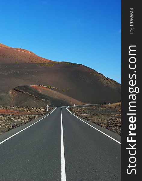 Quiet and empty road in the middle of the day at fool sun leading to Vulcan Timanfaya national park at Lanzarote Canary Islands. Quiet and empty road in the middle of the day at fool sun leading to Vulcan Timanfaya national park at Lanzarote Canary Islands