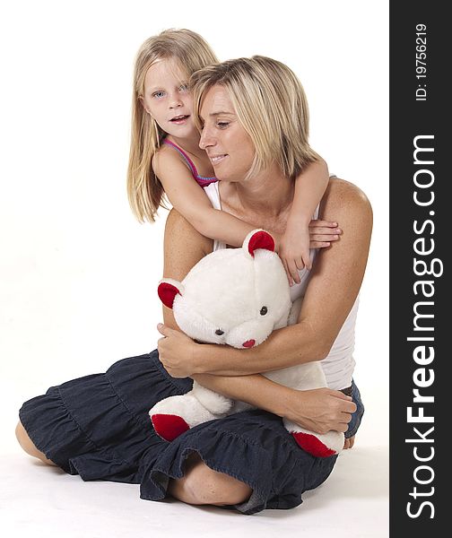 Attractive blonde mother and daughter, in a loving embrace, with a teddy bear. Attractive blonde mother and daughter, in a loving embrace, with a teddy bear.