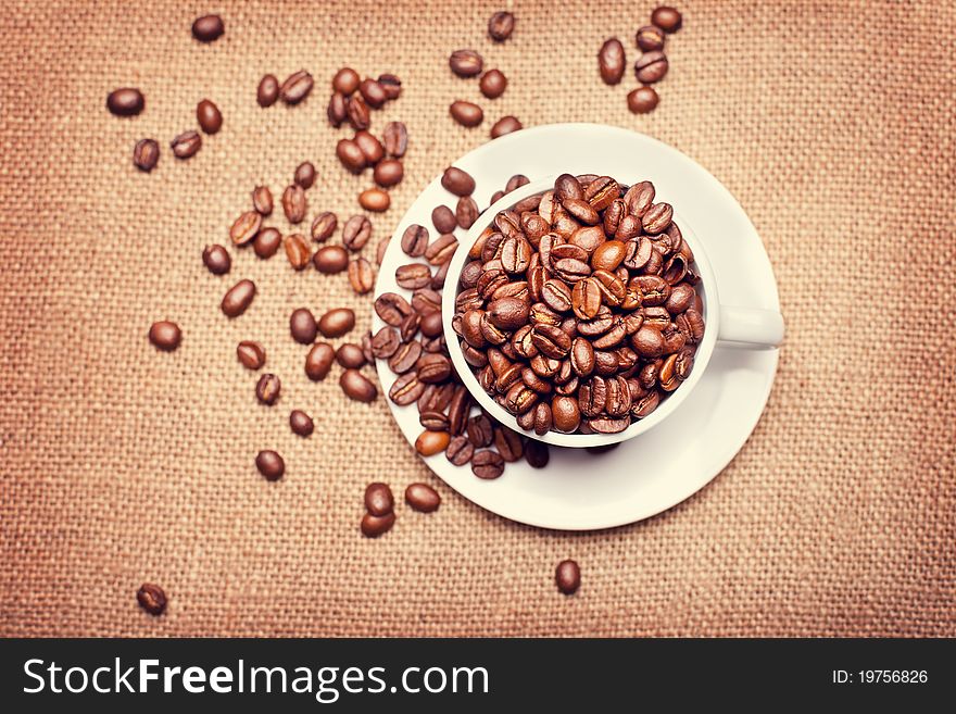 Cup with coffee beans on fabric texture background, top view