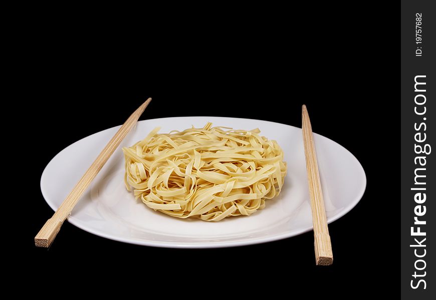 Uncooked noodles, on white plate, with chopsticks, isolated towards black background