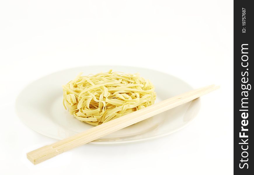 Dried uncoocked noodles, on white plate with chopsticks, isolated towards white background