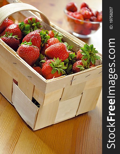 Fresh strawberries in basket on wooden table. In the background, a bowl of strawberries.