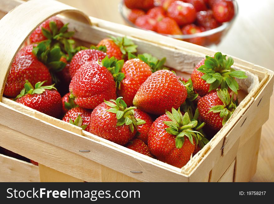 Strawberries in basket on wooden table. In the background, a bowl of strawberries.