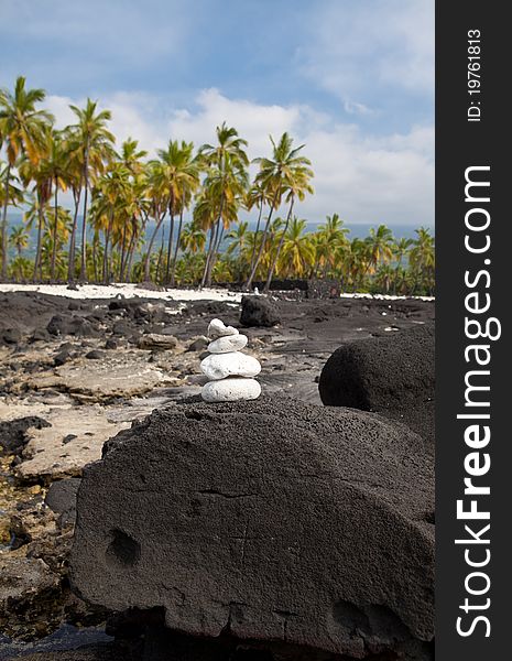 A photo of four balancing white stones sitting on a dark lava rock. Hawaiian landscape as background. A photo of four balancing white stones sitting on a dark lava rock. Hawaiian landscape as background.