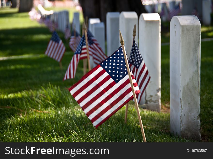 Headstones decorated with the American flag at a military cemetery. Headstones decorated with the American flag at a military cemetery.