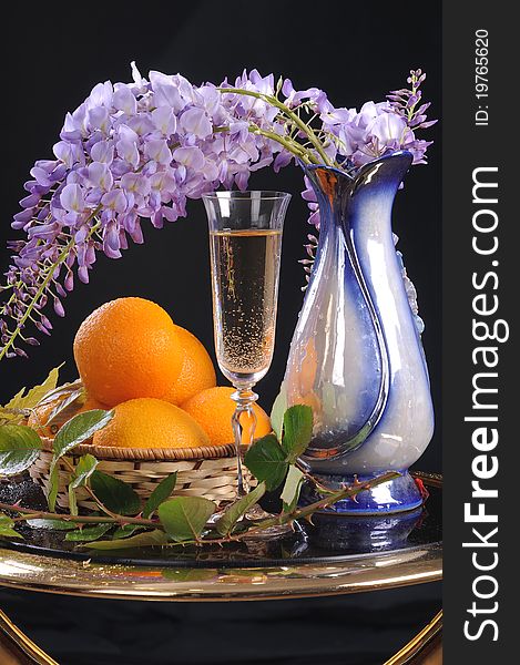 On a round little table a basket with oranges, white wine and a flower Wisteria. On a round little table a basket with oranges, white wine and a flower Wisteria.