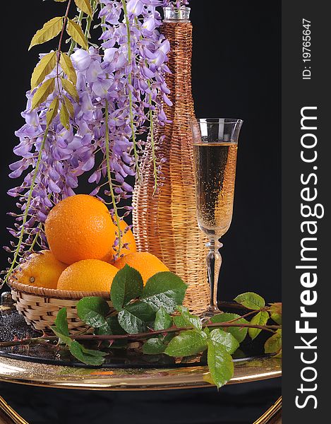 On a round little table a basket with oranges, white wine and a flower Wisteria. On a round little table a basket with oranges, white wine and a flower Wisteria.