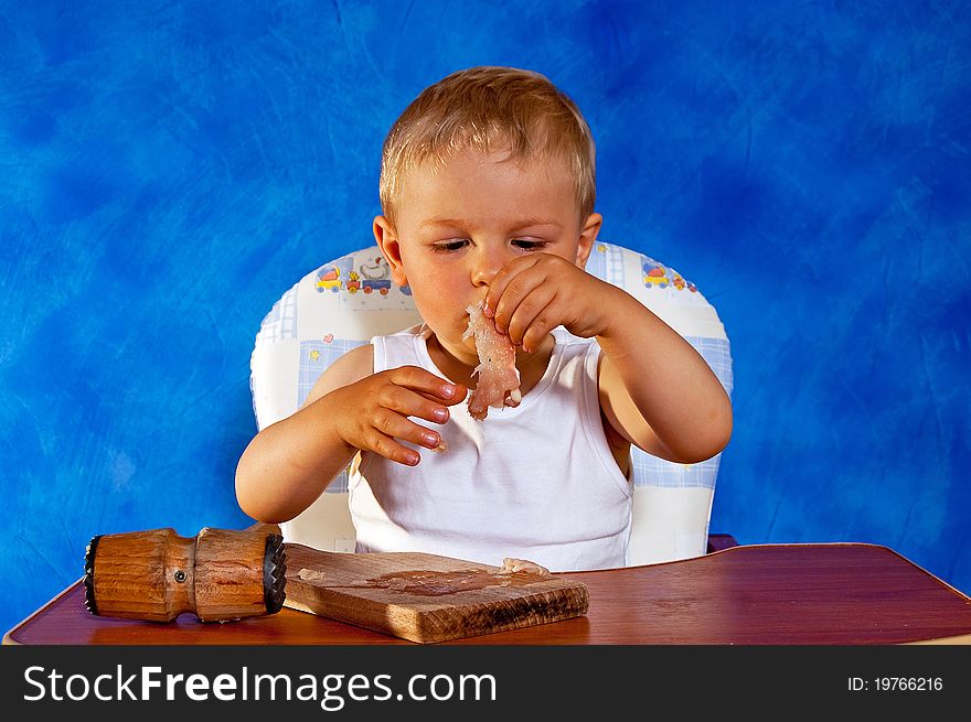 Short boy whipping cutlets with mallet after the board on the blue mosaic background