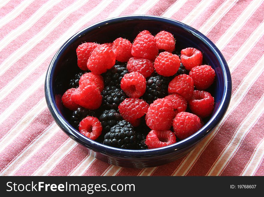 Blackberries and raspberries in a bowl on a striped placemat